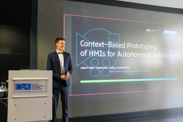 Lukas steht auf der Bühne während der Präsentation seiner Dissertation.