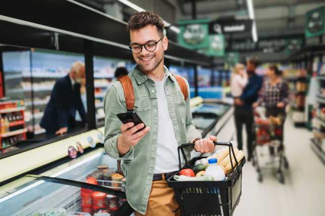 Junger Mann im Supermarkt schaut auf sein Smartphone.