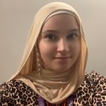 A woman wearing a beige hijab and leopard print top, standing against a plain background, with a lanyard around her neck.