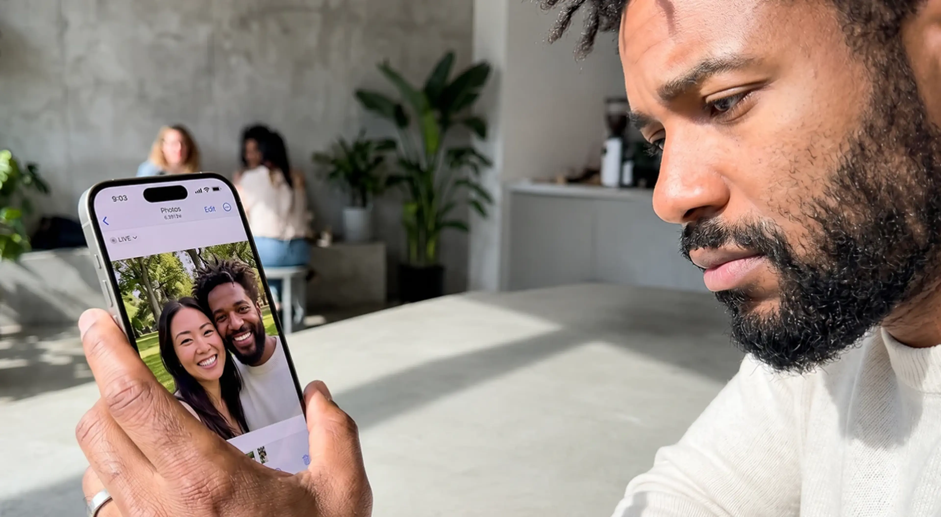 Sad Black man looking at a couples photo on his iPhone in a bright room with plants, representing grief after a break up