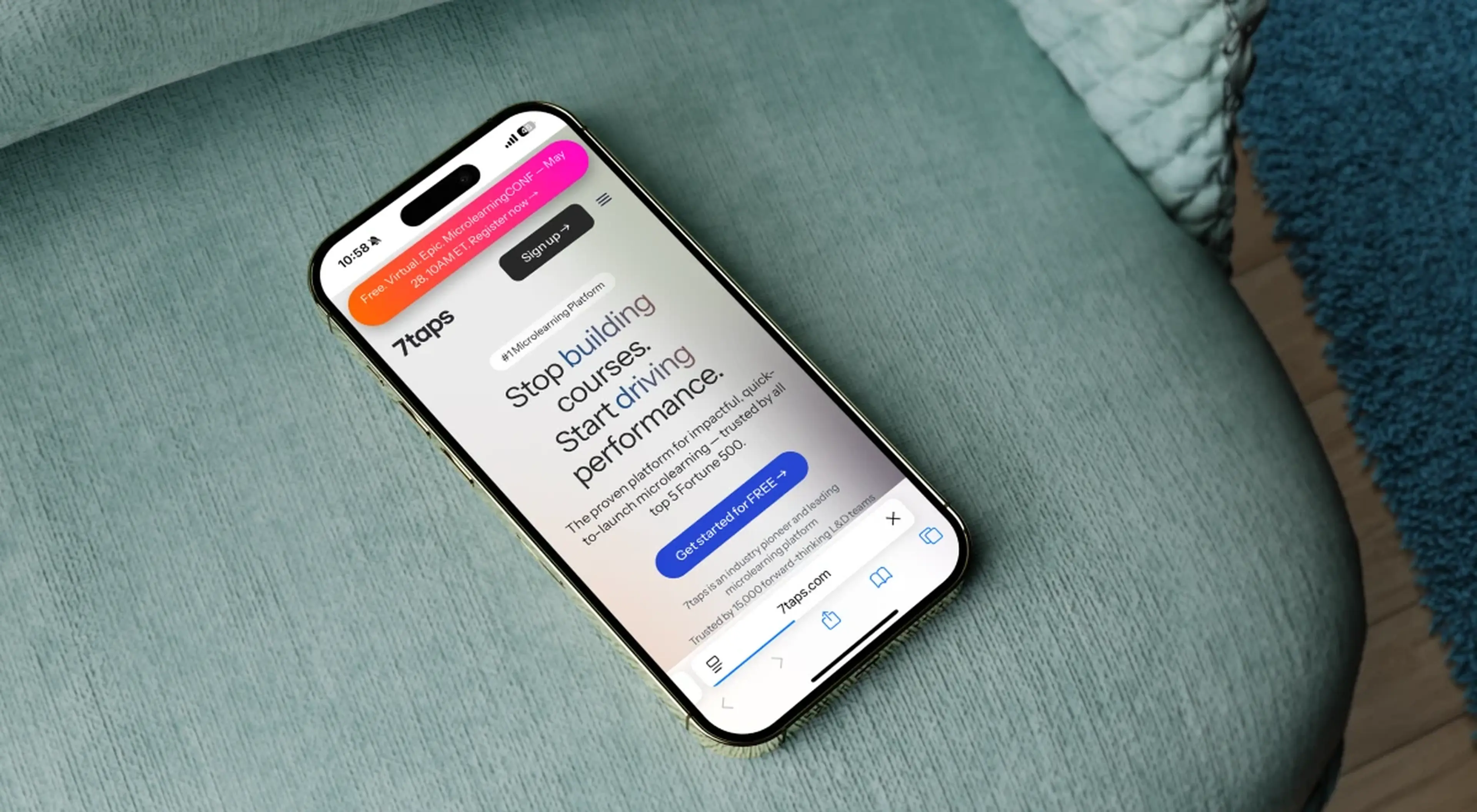 Smartphone resting on a teal couch displaying the 7taps microlearning platform website, shown as a 7taps alternative option for performance-driven corporate training