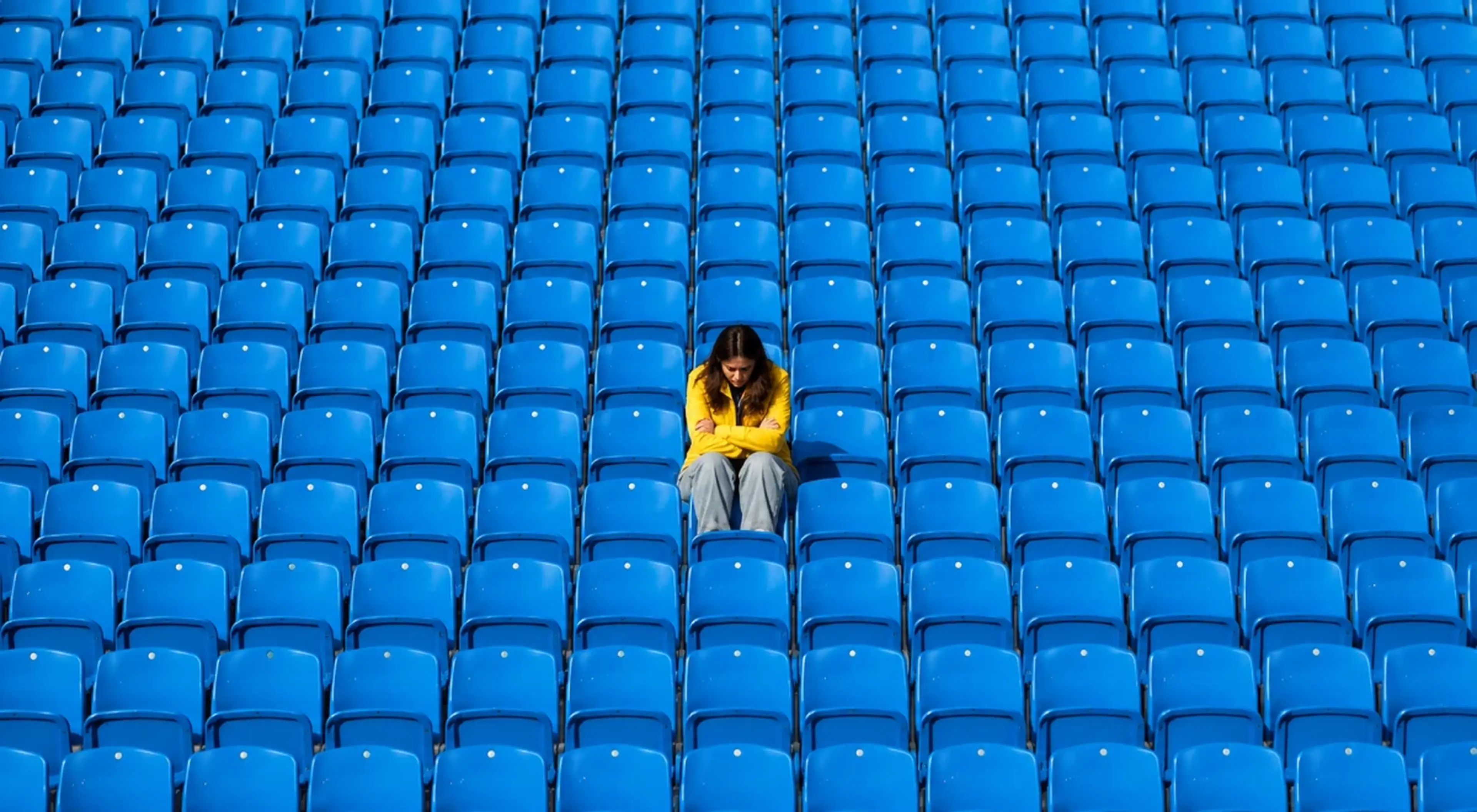 _Lonely person in a yellow hoodie sitting alone among rows of empty blue stadium seats, symbolizing loneliness and emotional isolation after a breakup