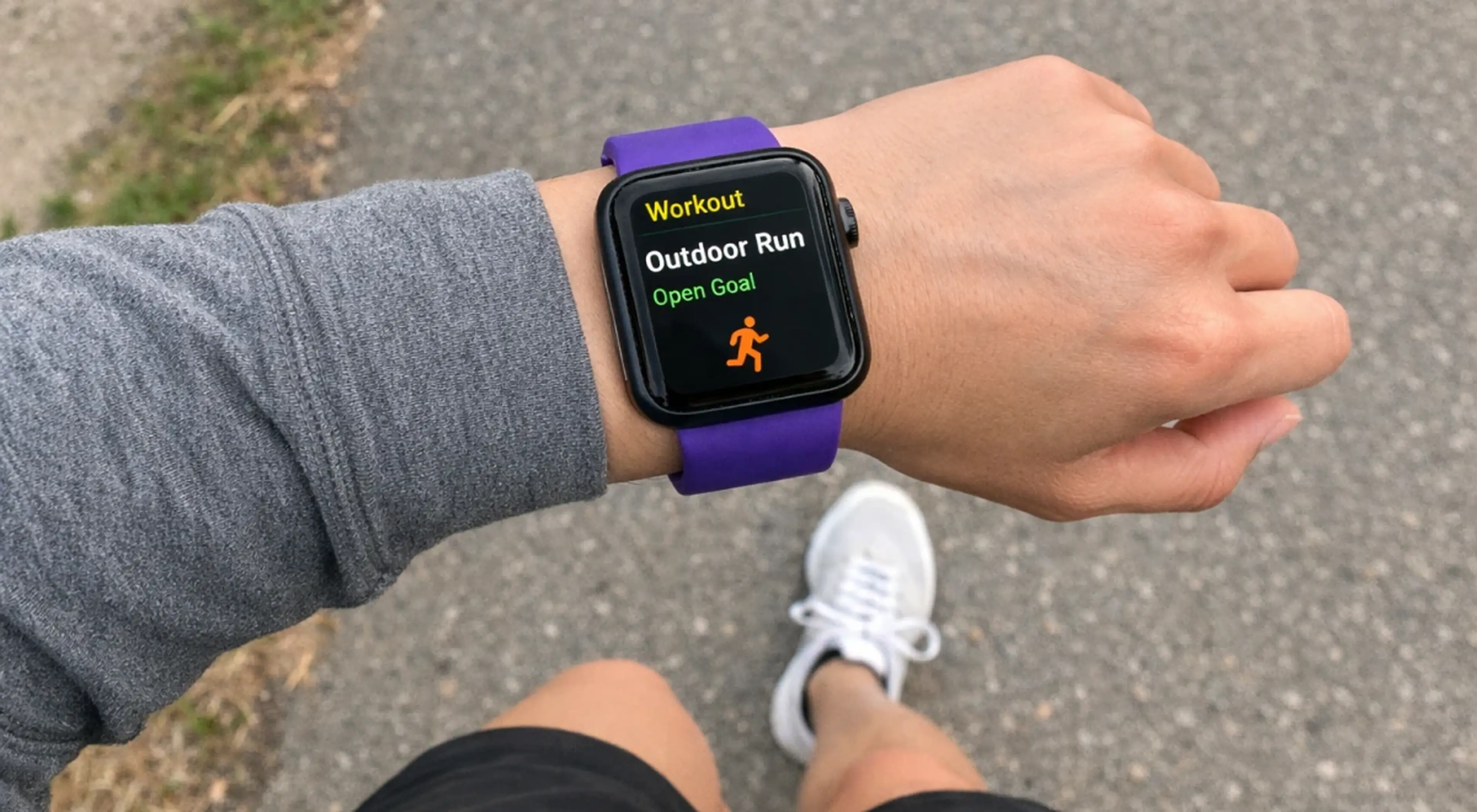 Person wearing Apple Watch with purple band displaying Outdoor Run workout on pavement, reflecting David Goggins daily routine built on mental toughness and discipline
