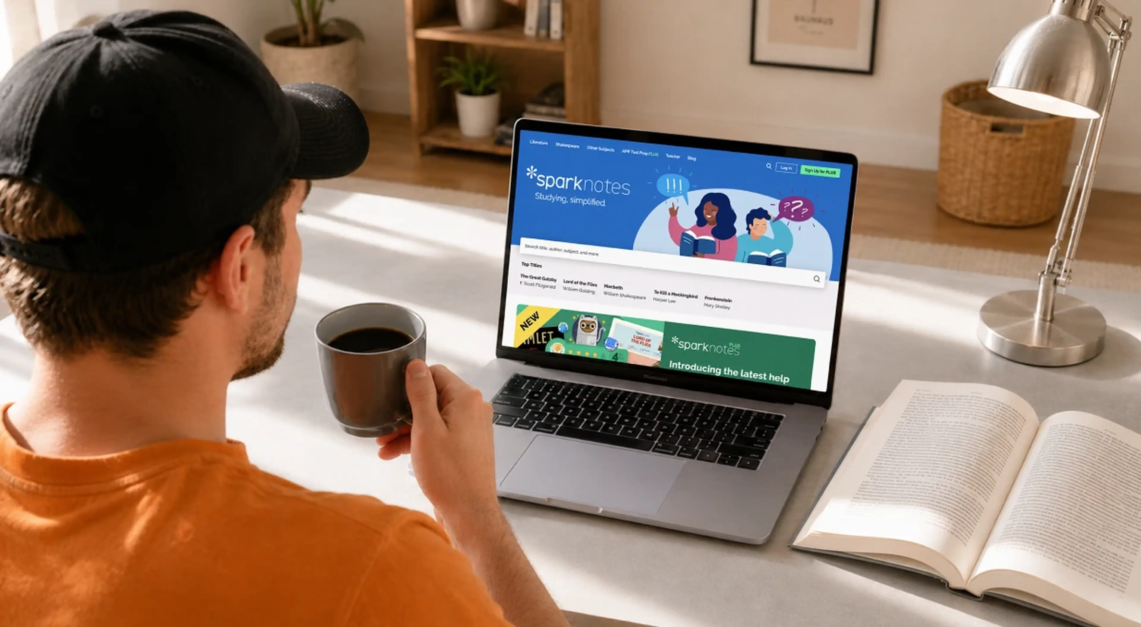 Young man in an orange hoodie holding a coffee mug while browsing the SparkNotes website on a laptop, with an open book and desk lamp nearby