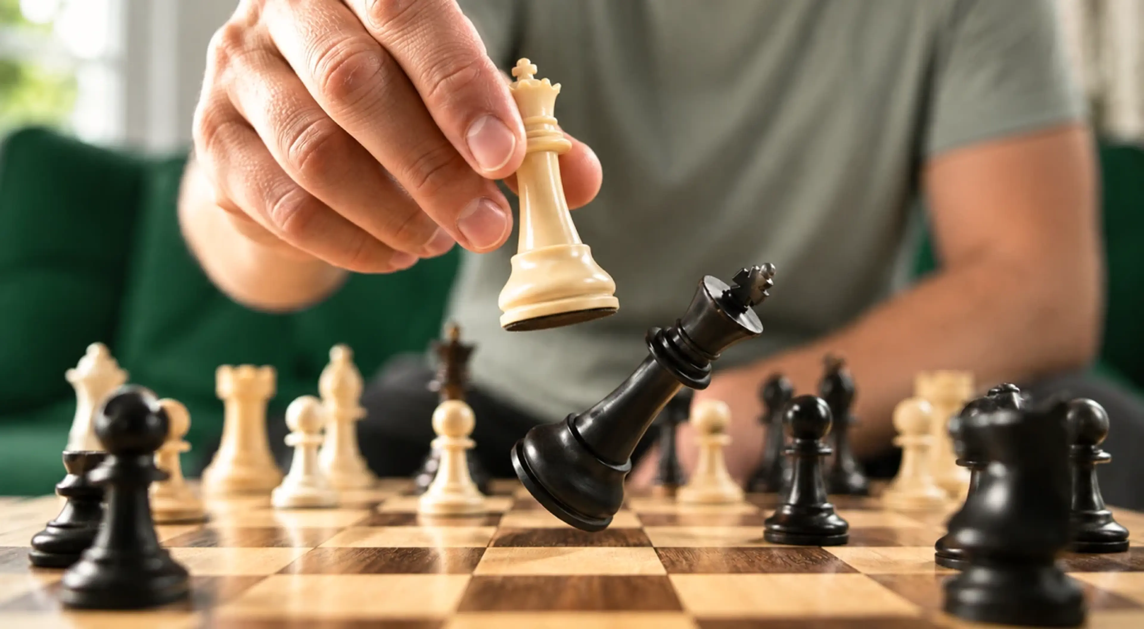 Person moving a white chess piece on a wooden chessboard during a strategic game, representing critical thinking and learning habits