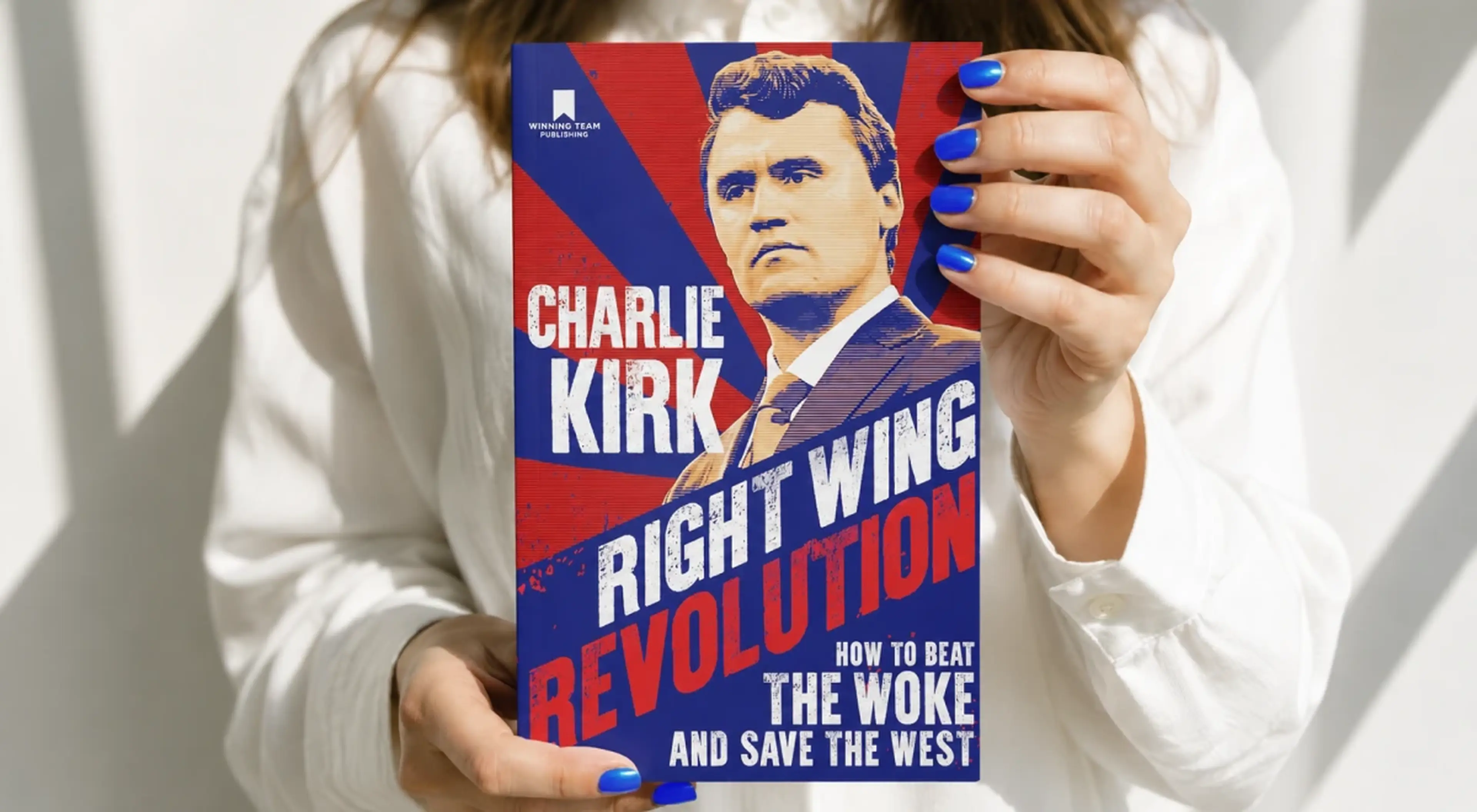 Woman in a white shirt with blue nails holding Charlie Kirk's book _Right Wing Revolution_ against a light background
