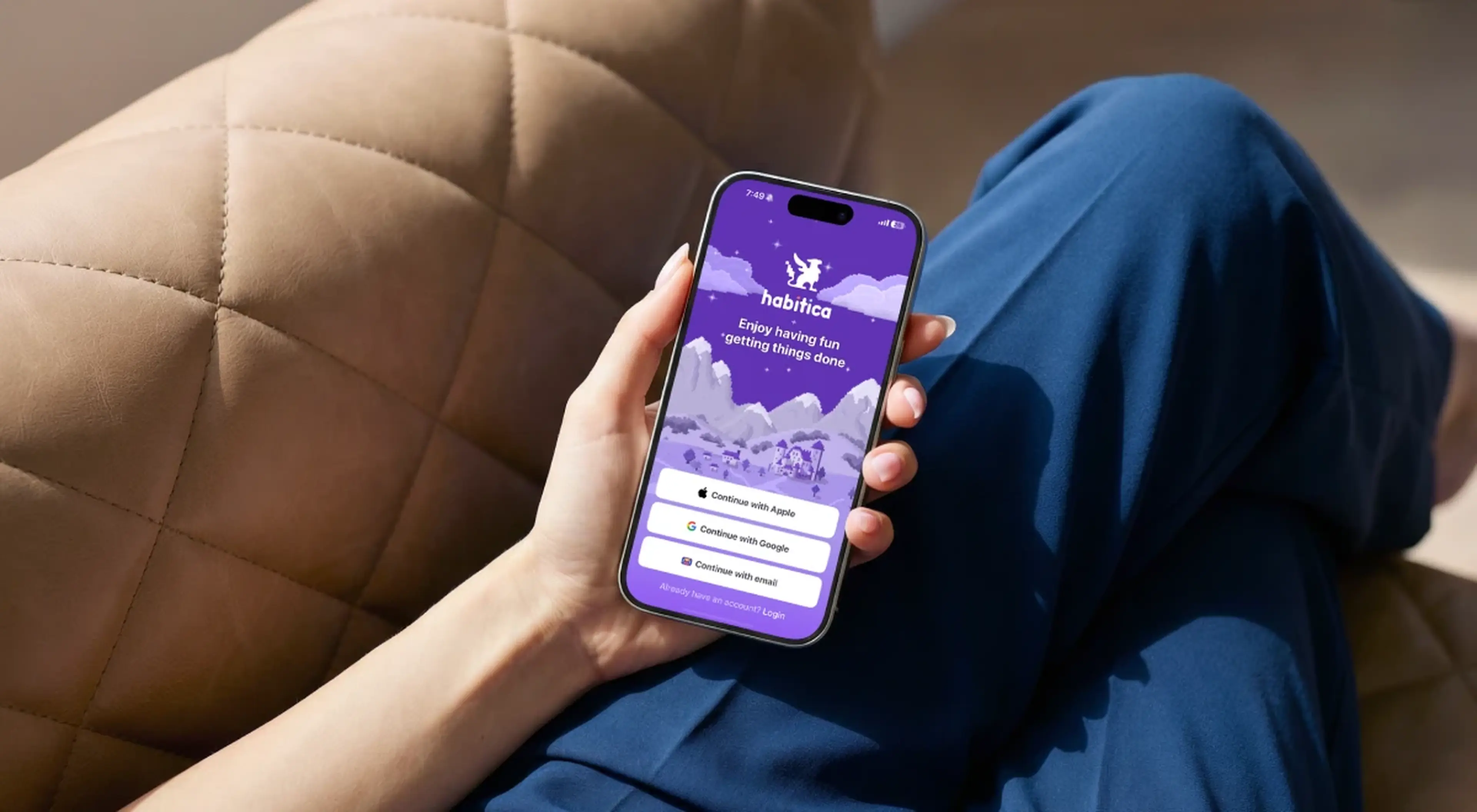 Person relaxing on a beige couch holding a smartphone with the Habitica app open, wearing blue pants, with a purple-themed gamified habit tracker screen visible