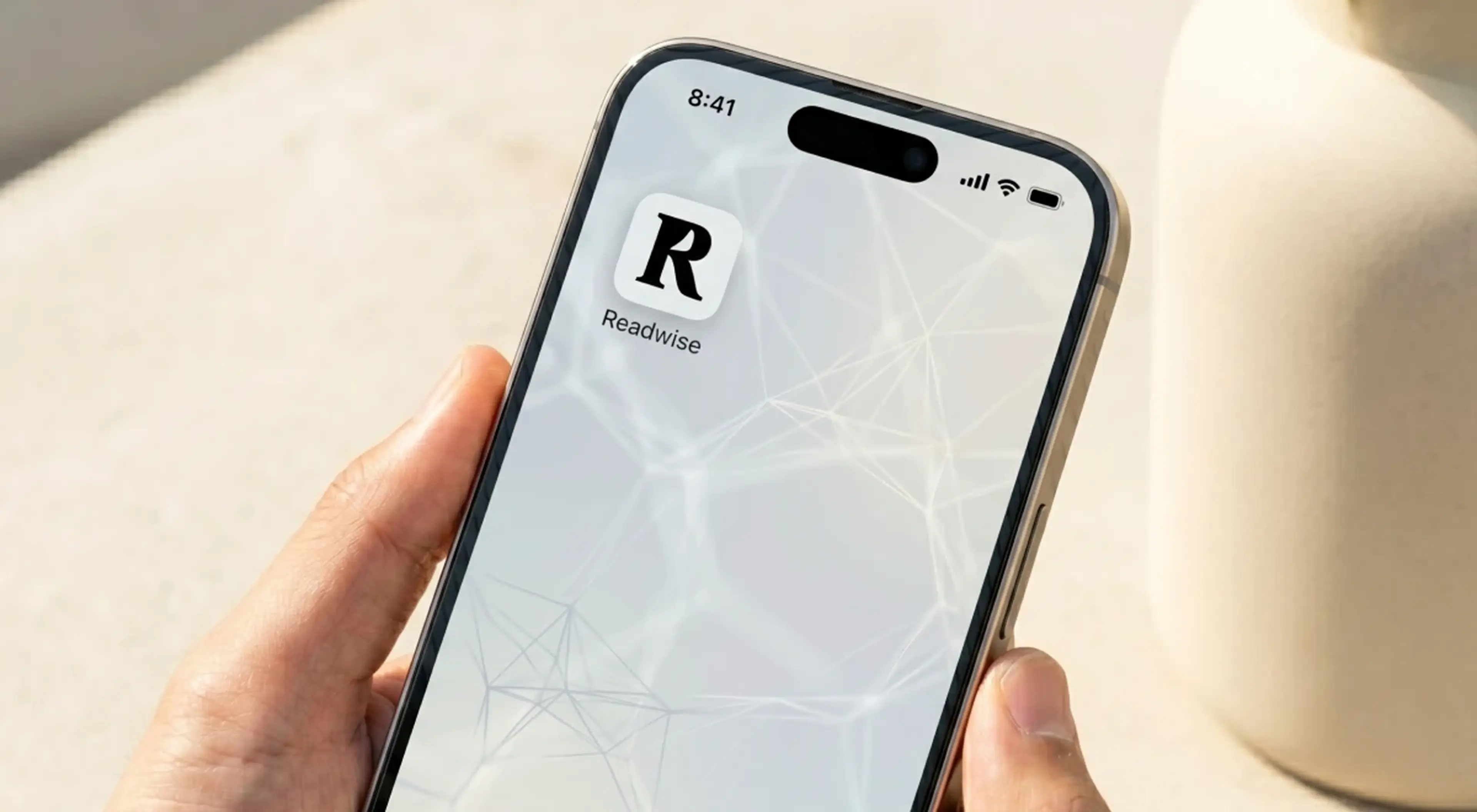 Hand holding a smartphone displaying the Readwise app home screen with a map-style interface, against a soft beige background (1)