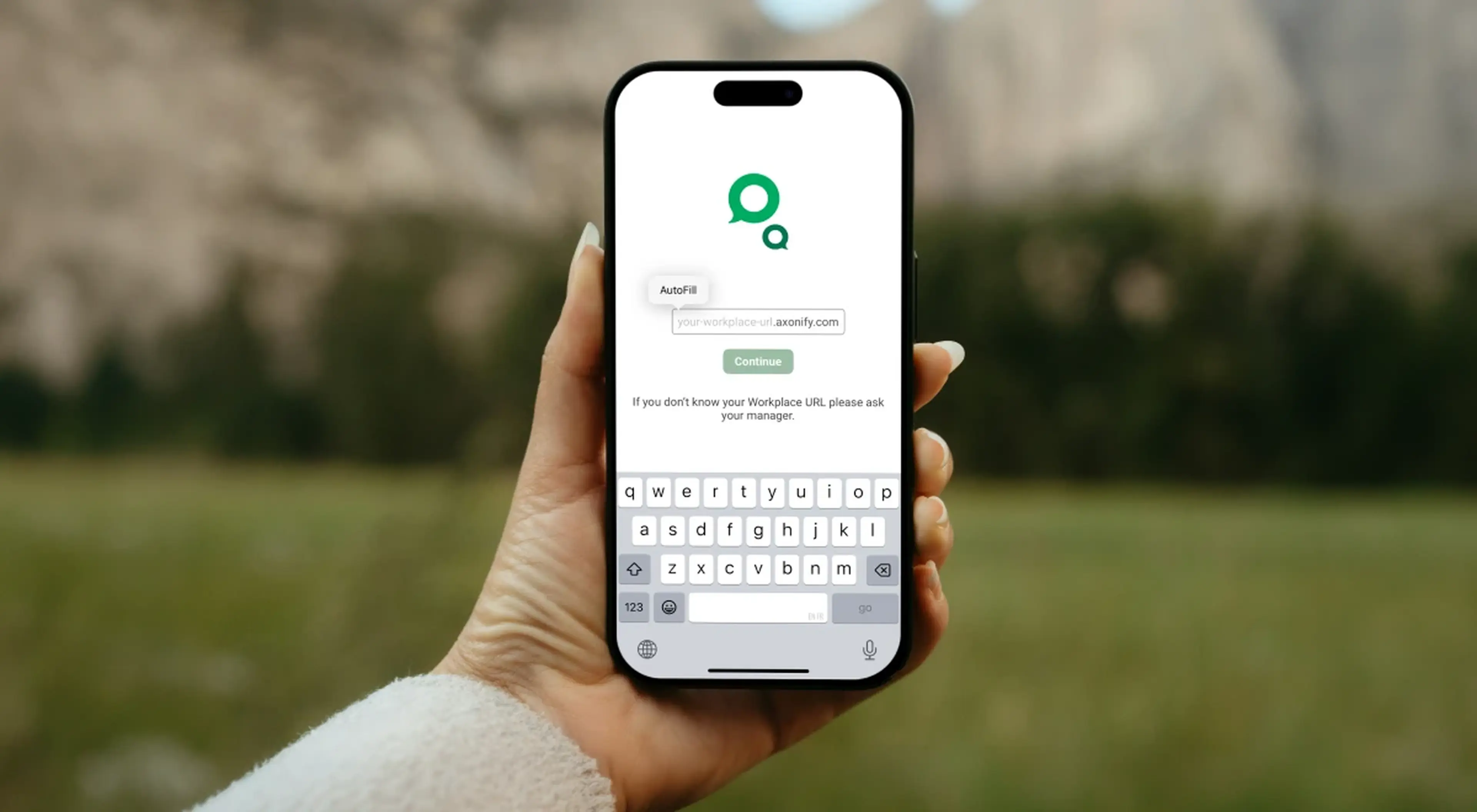 Hand holding a smartphone displaying the Axonify app login screen with a mountain landscape in the background
