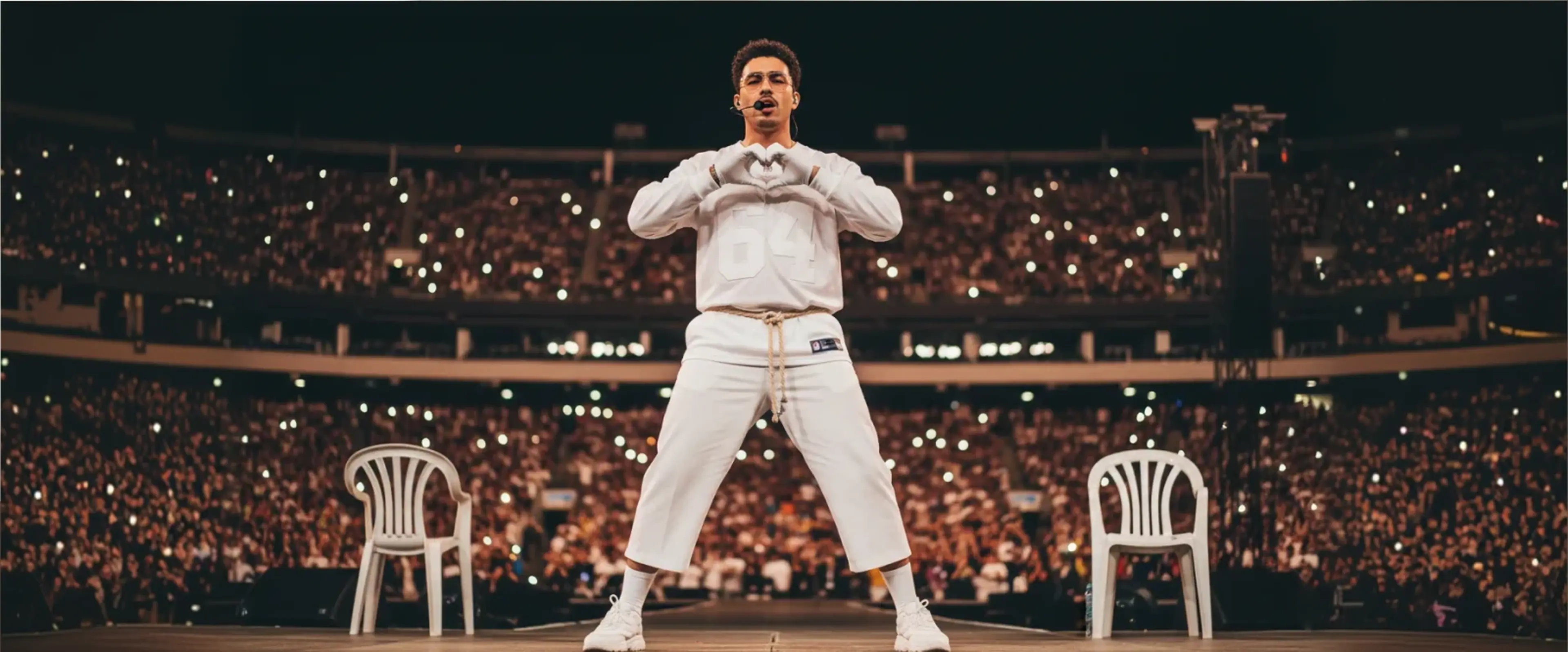 Bad Bunny performing on stage in white outfit making heart gesture to crowd at packed stadium during Super Bowl halftime show