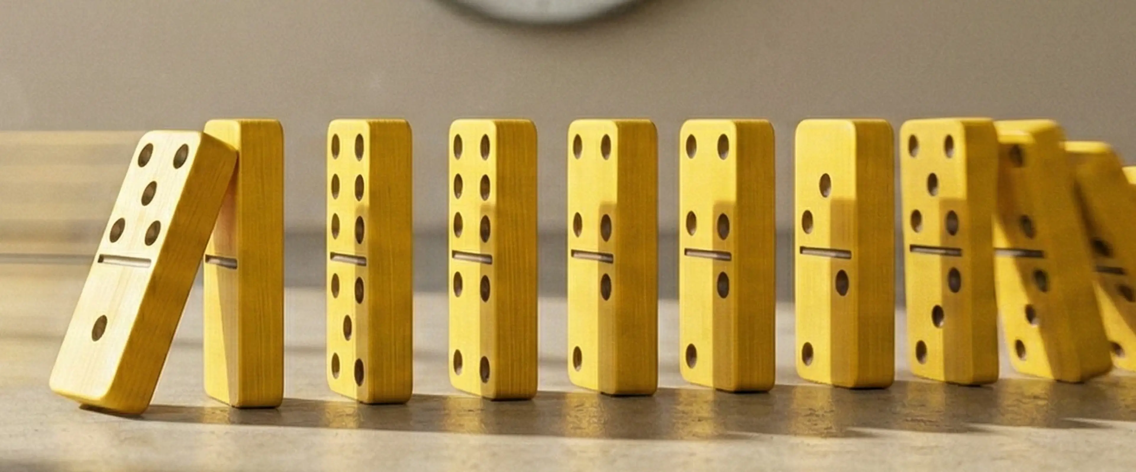 Yellow dominoes falling in a chain reaction on a concrete surface, with a wall clock in the background, symbolizing time management and the productivity impact of tracking weekly habits