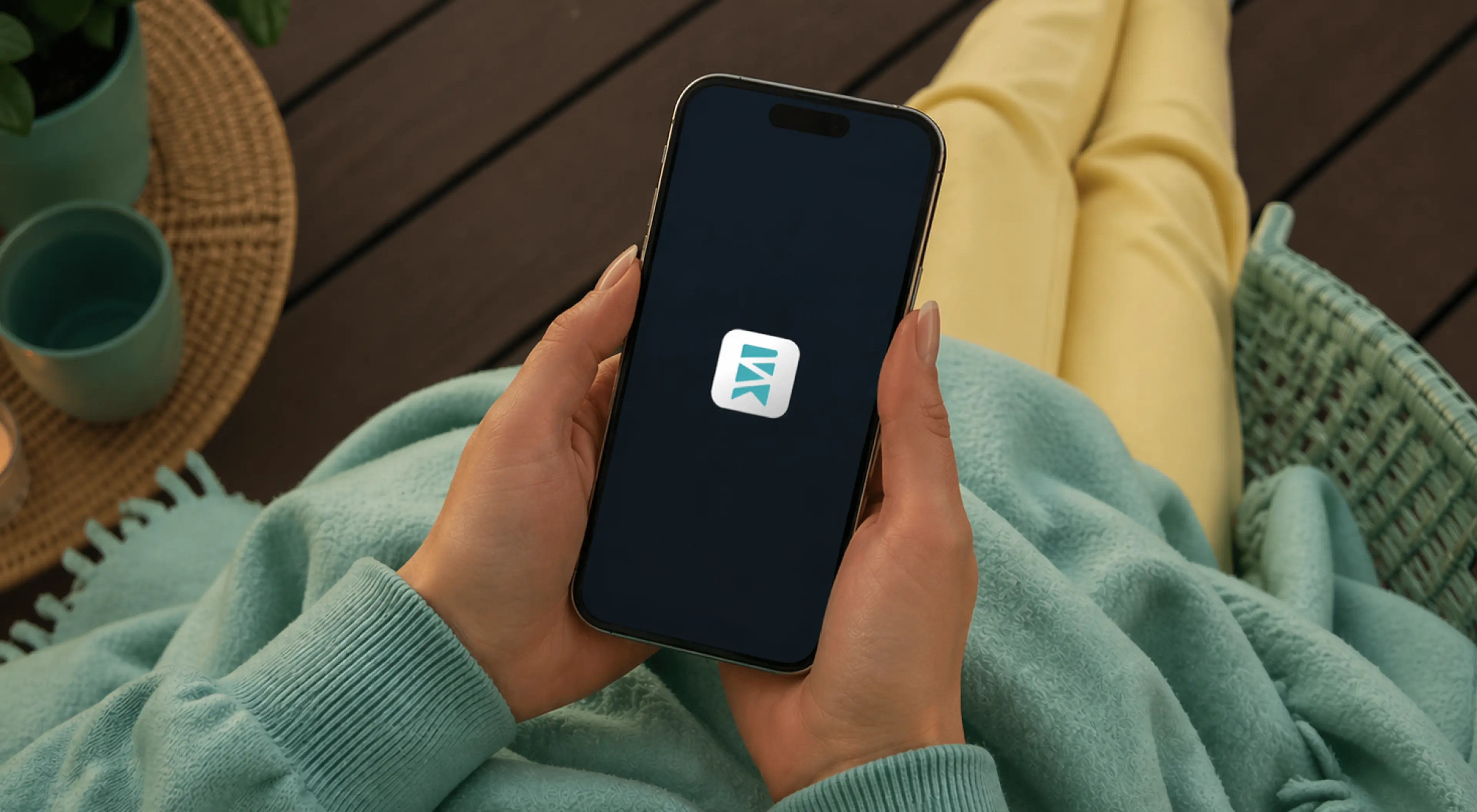 Hand holding a smartphone displaying the SuperSummary app icon while relaxing outdoors on a teal blanket, representing a deep study app review
