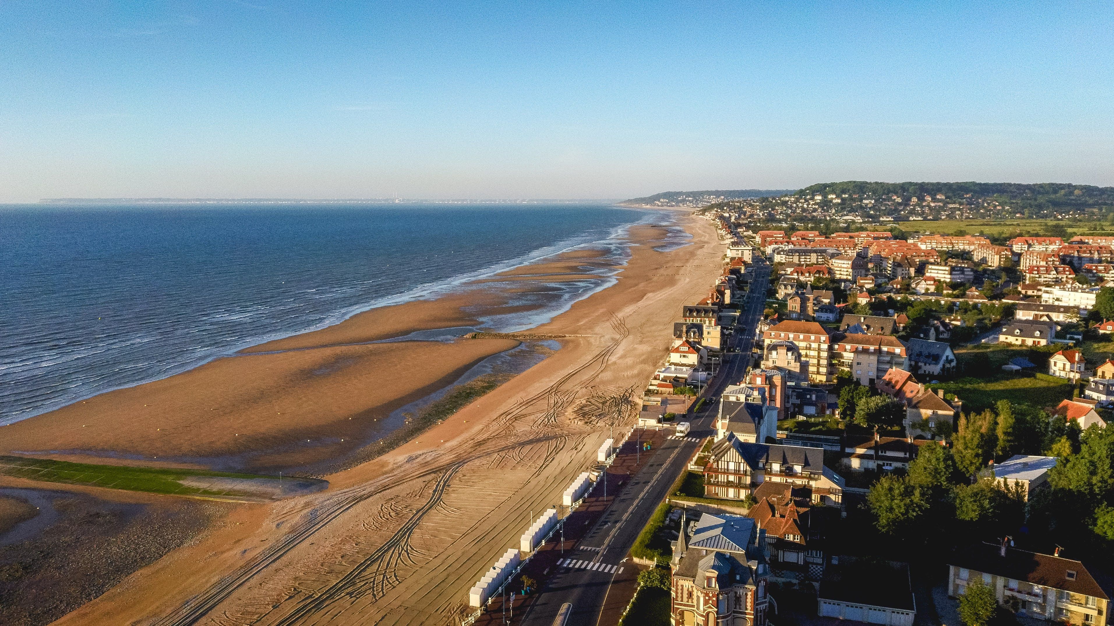 Luchtfoto van een kuststad met zandstranden, oceaangolven en woongebouwen onder een helderblauwe hemel.