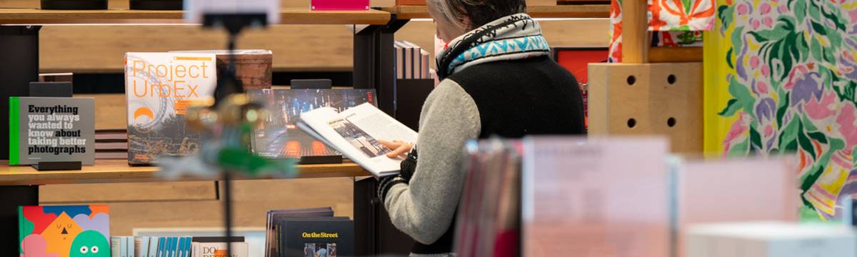 Person browsing a book in a colourful bookstore, surrounded by various titles and vibrant displays.