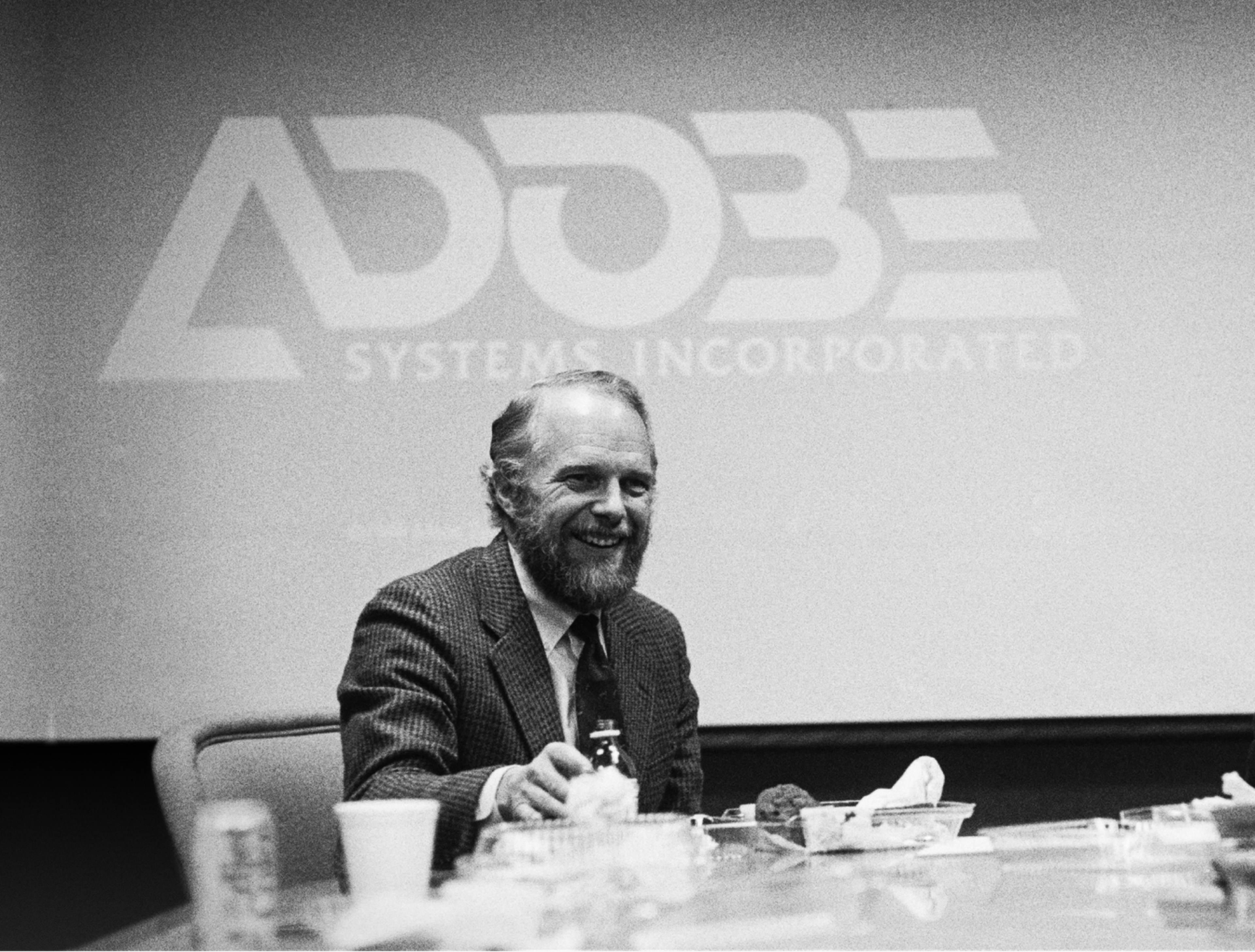 John Warnock infront of the first iteration of the Adobe logo