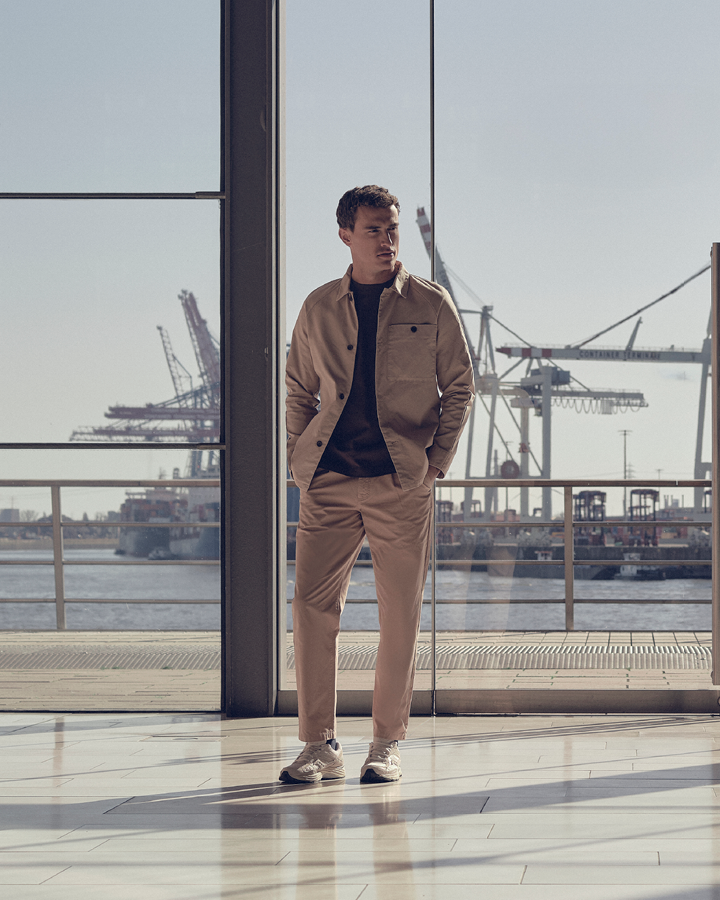 Man gekleed in een beige overshirt, een bruin T-shirt en een beige broek