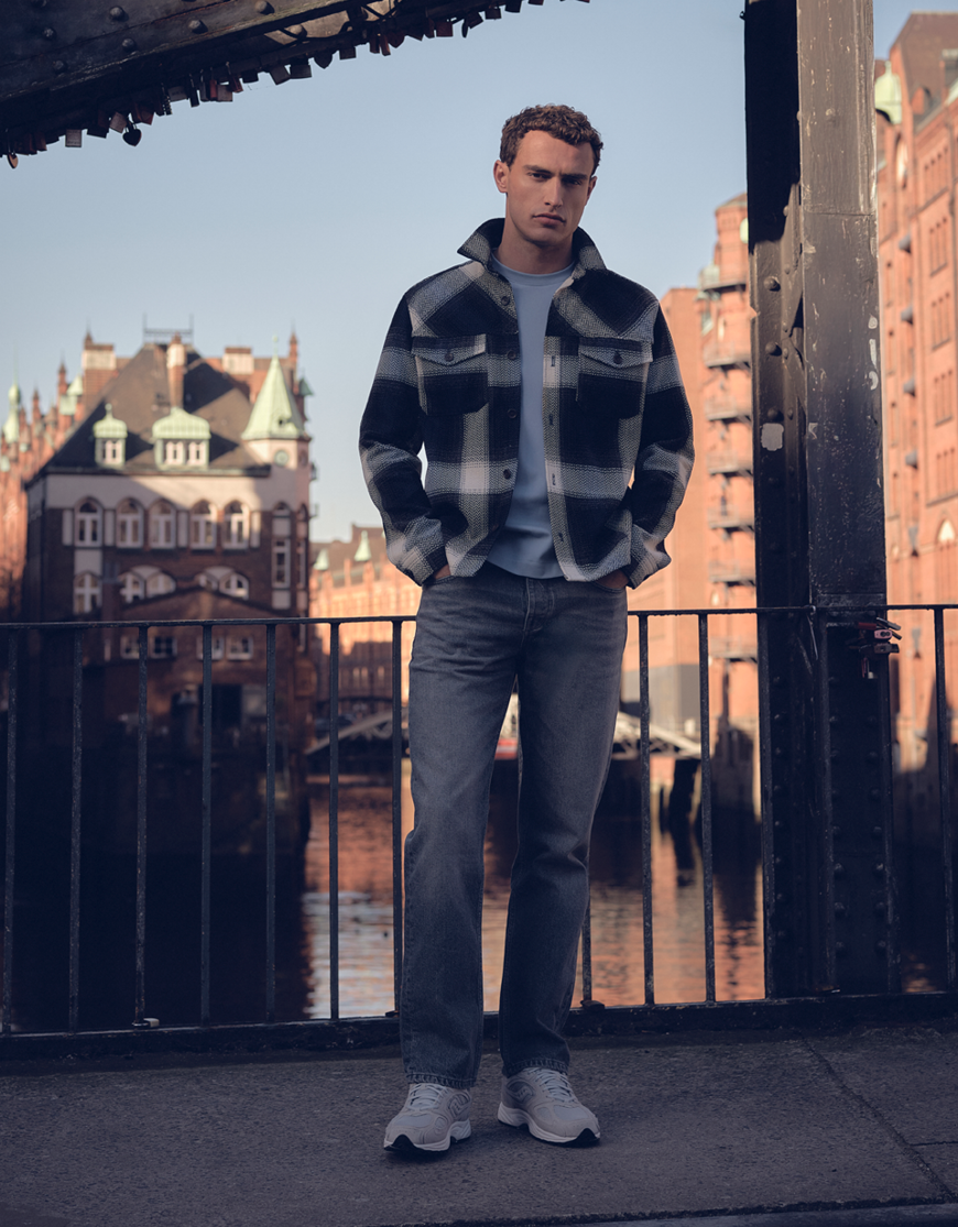 Man gekleed in een geruit overshirt, een licht blauw T-shirt en een grijze jeans