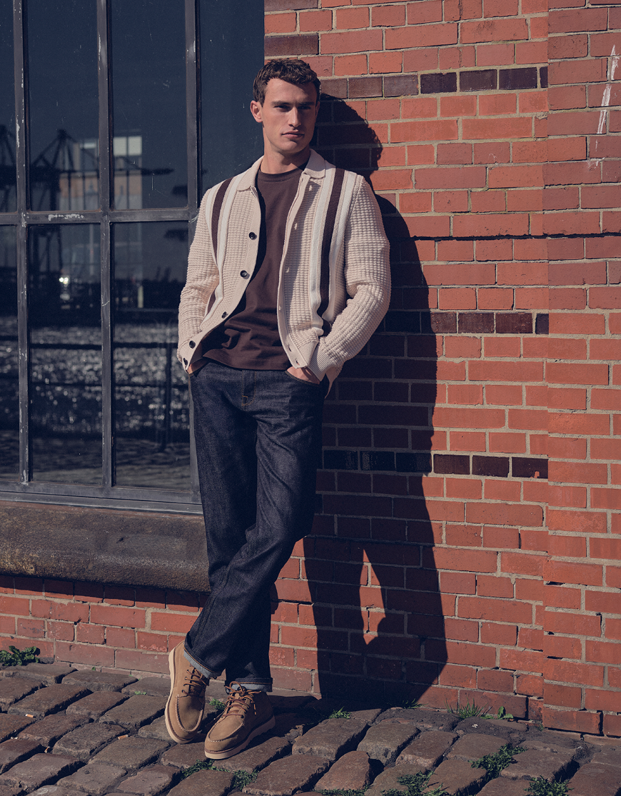 Man gekleed in een beige polo, een bruin T-shirt een een jeans