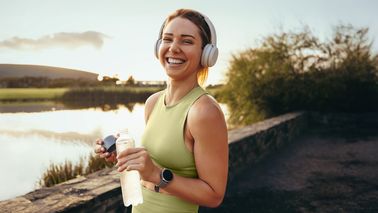 Läuferin lächelt nach dem Training mit Kopfhörern und Wasserflasche – Symbolbild für Regeneration mit Protein, Magnesium, Kohlenhydraten und Schlaf.