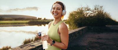 Läuferin lächelt nach dem Training mit Kopfhörern und Wasserflasche – Symbolbild für Regeneration mit Protein, Magnesium, Kohlenhydraten und Schlaf.