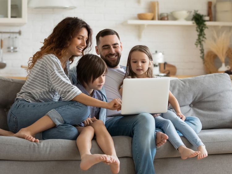 Familie sitzt mit einem Laptop auf dem Sofa