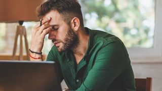 Mann sitzt am Schreibtisch und wirkt gestresst. 