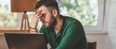 Mann sitzt am Schreibtisch und wirkt gestresst. 