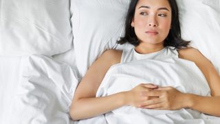 Frau liegt im Bett und hat Symptome von Schlafstörungen.