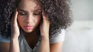 Junge Frau ist nervös und fasst sich mit den Händen an die Schläfen.