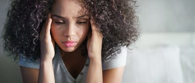 Junge Frau ist nervös und fasst sich mit den Händen an die Schläfen.