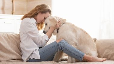 Frau sitzt mit Hund auf der Couch.