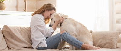 Frau sitzt mit Hund auf der Couch.