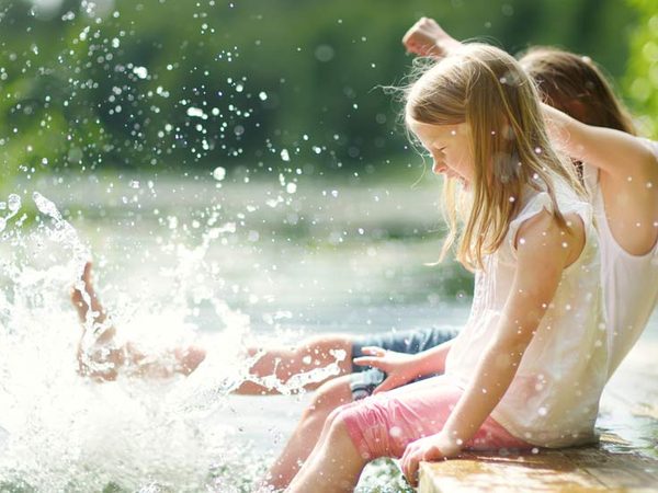 Kinder sitzen am Wasser und haben die Füße im See