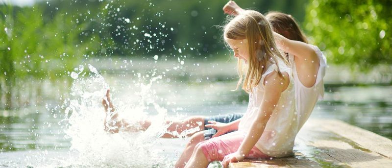 Kinder sitzen am Wasser und haben die Füße im See