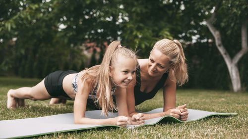 Mutter und Tochter sind im Garten und machen einen Plank auf einer Yogamatte.