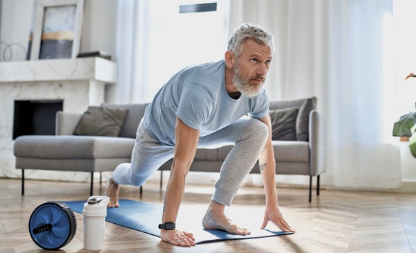 Mann wärmt sich auf eine Matte zuhause für HIIT auf.
