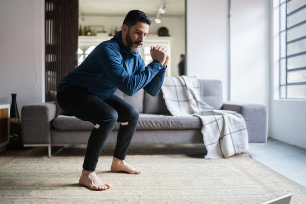 Mann macht im Wohnzimmer eine tiefe Kniebeuge