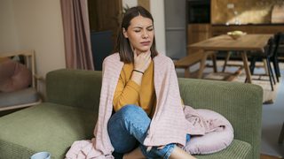 Frau mit Halsschmerzen sitzt auf dem Sofa