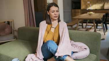 Frau mit Halsschmerzen sitzt auf dem Sofa
