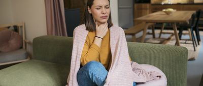 Frau mit Halsschmerzen sitzt auf dem Sofa