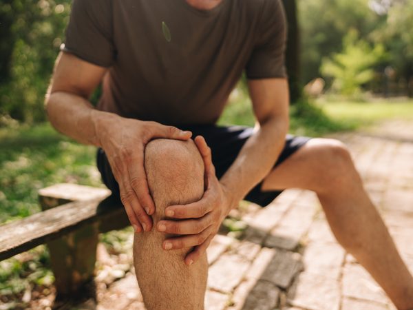 Mann hält sich das Kniegelenk – Symbol für Gelenkschmerzen