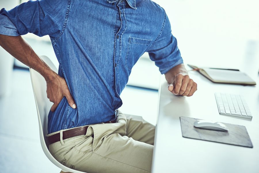 Mann sitzt am Schreibtisch und fasst sich an den unteren Rücken
