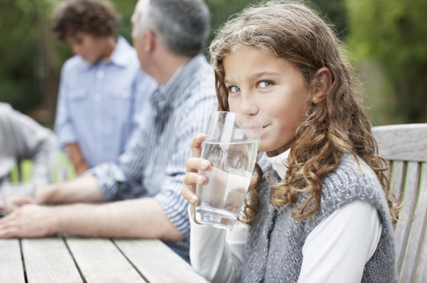Ein Mädchen sitzt draußen am Tisch und trinkt ein großes Glas Wasser