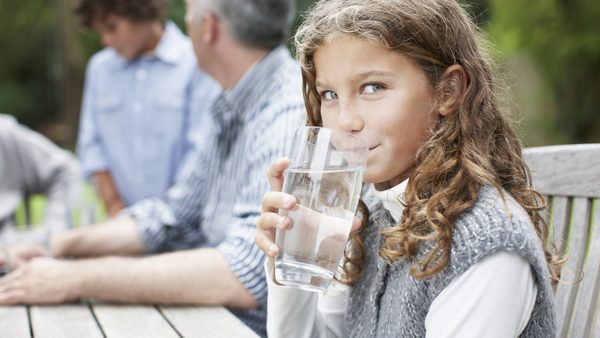 Mädchen trinkt Wasser am Familientisch; Wasser statt Süßgetränke kann helfen, einer Fettleber vorzubeugen.