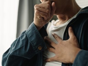Person hält sich mit einer Hand an den Brustbereich als Darstellung von Sodbrennen