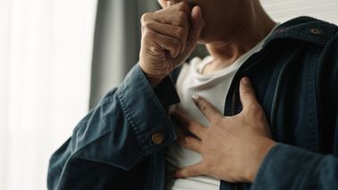 Person hält sich mit einer Hand an den Brustbereich als Darstellung von Sodbrennen
