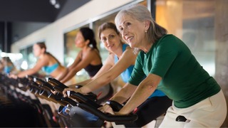 Frauen sitzen auf Ergometern.
