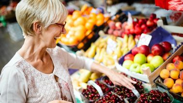 Frau kauft auf Markt frisches Obst und Gemüse ein.