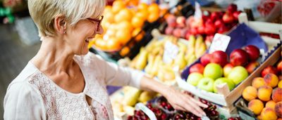 Frau kauft auf Markt frisches Obst und Gemüse ein.