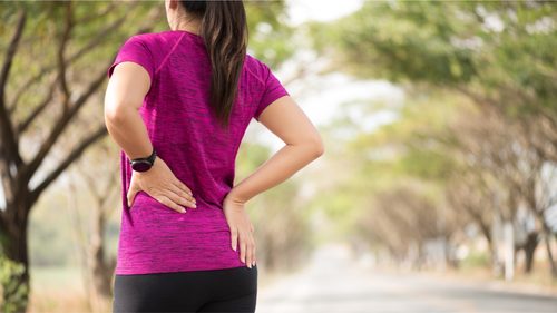 Frau in Sportkleidung fasst sich an den unteren Rücken